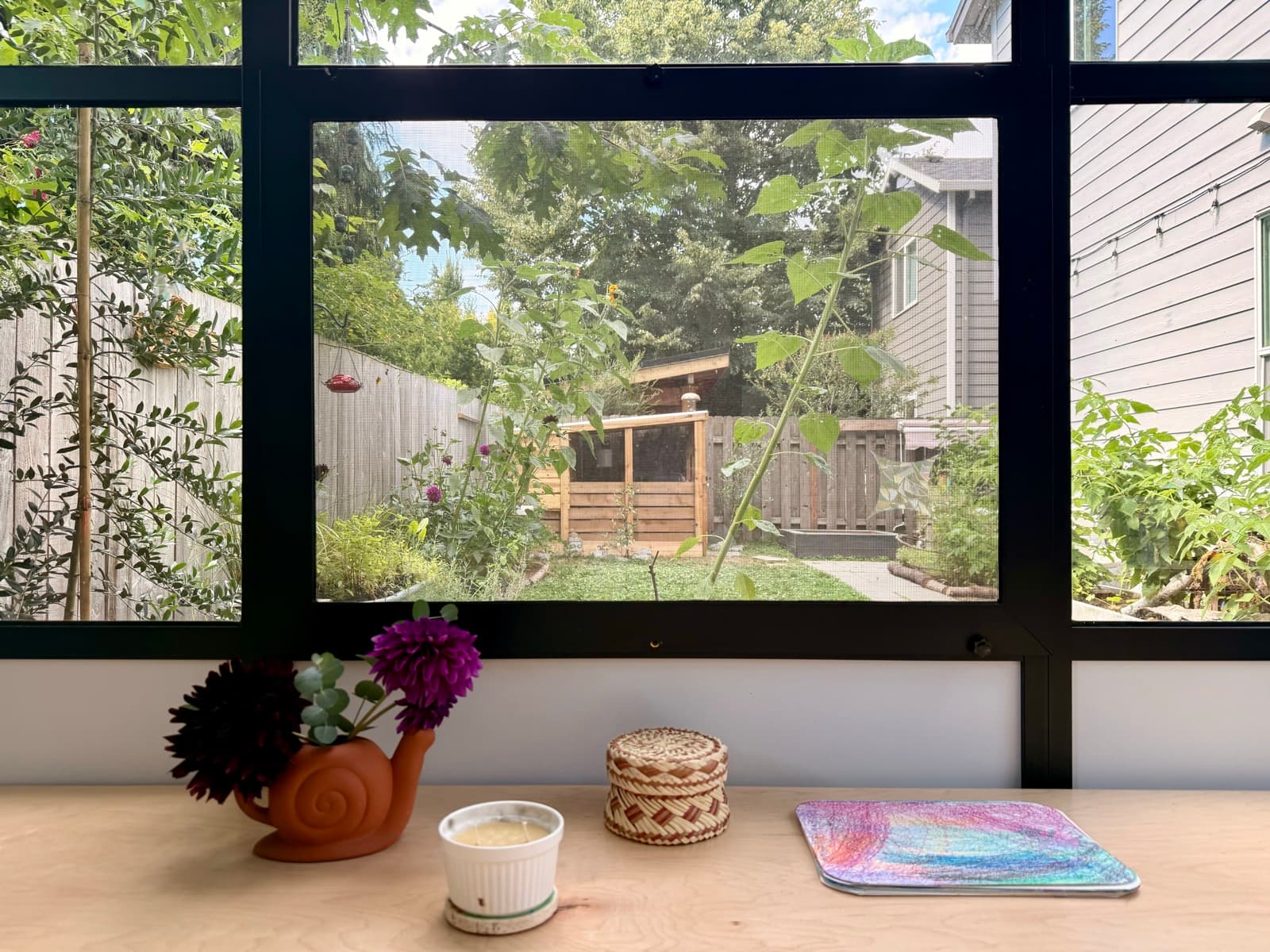 A window seat with fresh dahlias, a candle, and a finished piece of art